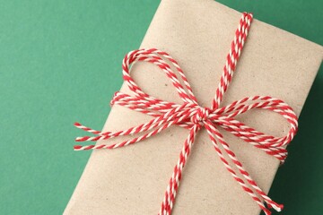 Gift wrapped in kraft paper with bow on green background, top view