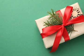 Gift wrapped in kraft paper with bow, ornament and fir tree branch on green background, top view....