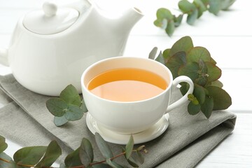Aromatic tea in cup and eucalyptus branches on white wooden table, closeup