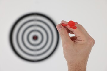 Targeting. Man with arrow aiming at dart board on light background, closeup