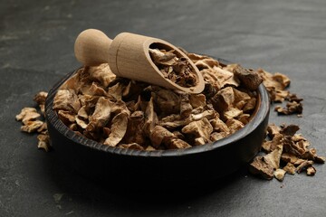 Pieces of dry chicory roots in bowl and scoop on dark textured table, closeup