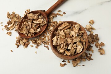 Pieces of dry chicory roots in bowl and spoon on white table, flat lay