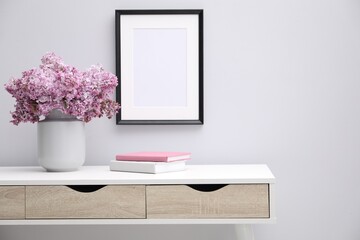 Beautiful lilac flowers in vase, books and picture frame indoors