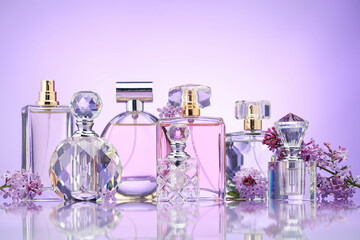 Bottles of perfume and lilac flowers on mirror surface against violet gradient background