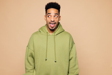Young surprised shocked man of African American ethnicity wear green hoodie casual clothes look aside on area mock up isolated on plain pastel light beige background studio portrait Lifestyle concept