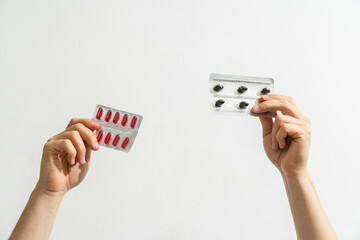 Hands holding red and black pills in blister packs on white background