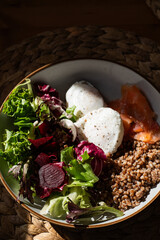 Homemade healthy and balanced breakfast from buckwheat, smoked salmon, salad leaves, beetroot, and poached eggs. Breakfast with strong sun light and shadows