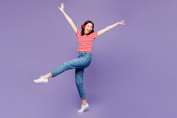 Full body young woman wear red striped t-shirt casual clothes listen to music in headphones raise...