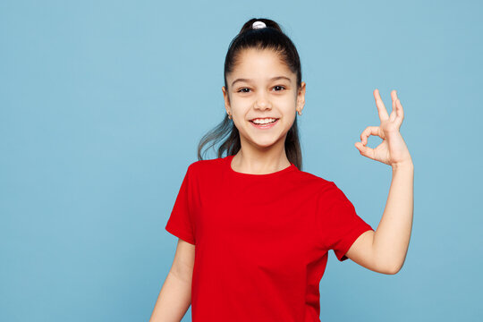 Little happy kid girl 8-9 years old wears red t-shirt have fun showing okay ok gesture isolated on pastel light blue color background child studio portrait. Mother's Day love family lifestyle concept.
