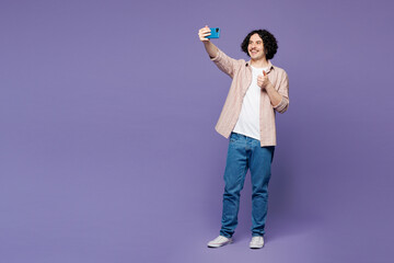 Full body young man he wears pink shirt t-shirt casual clothes doing selfie shot on mobile cell phone post photo on social network show thumb up isolated on plain purple background. Lifestyle concept. © ViDi Studio