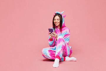 Full body young woman she wearing domestic costume with hoody and animal ears sit hold in hand use mobile cell phone isolated on plain pastel light pink background studio portrait. Lifestyle concept.