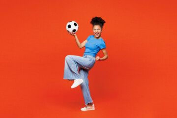 Full body side view young woman fan wear blue t-shirt cheer up support football sport team hold soccer ball watch tv live stream do winner gesture clench fist isolated on plain red orange background.