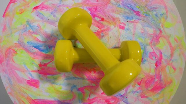 Top view. Vinyl dumbbell yellow 1 kg weight, on a rotary table, sports dumbbell spins. On a colorful stylish background.