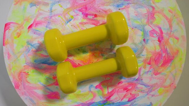 Top view. Vinyl dumbbell yellow 1 kg weight, on a rotary table, sports dumbbell spins. On a colorful stylish background.