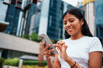 A young woman is engrossed in using her smartphone while situated in an urban environment