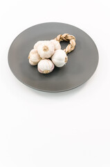 immagine raffigurante una treccia di aglio essicato su piatto in ceramica grigio, sfondo bianco