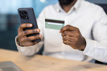 A person holds a smartphone and a credit card, potentially for online payment or transactions. The individual's hands are prominent.