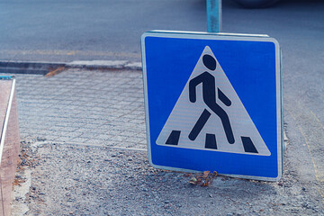 A road sign indicating a place for a pedestrian crossing slid down onto the sidewalk. The symbolism...