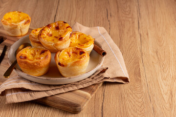 Pastel de Nata - Traditional portuguese egg custard pies left on wooden background, plate composition leaves right space clean. Portuguese pastries on a ceramic plate