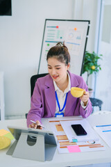 Happy attractive Asian businesswoman working on laptop and holding coffee cup with smile in Modern office or living room with copy space,E-commerce,internet technology, startup small business concept