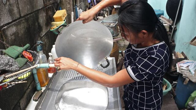 A woman washes dishware in an outdoor sink