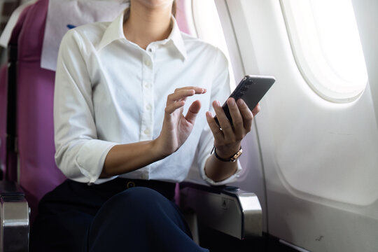 Business Travel. Professional woman using smartphone while seated on an airplane.
