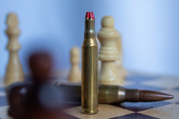 A pair of rifle bullets positioned on a chessboard in front of chess pieces represents the...