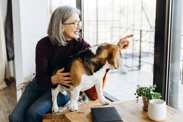 Smiling senior woman showing something through window to her beagle dog