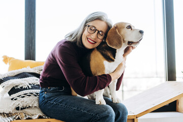 Smiling retired woman hugging beagle dog at home