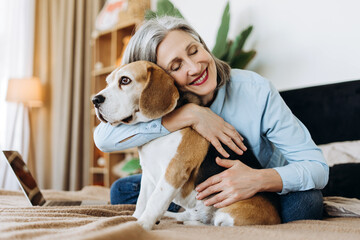 Senior woman hugging beagle dog at home on bed