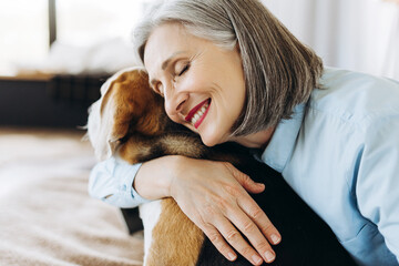 Happy senior woman hugging beagle dog at home: showing love and affection