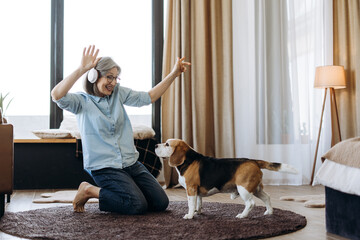 Happy senior woman listening music with headphones and dancing with beagle dog at home