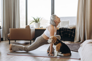 Senior woman practicing yoga with her beagle at home