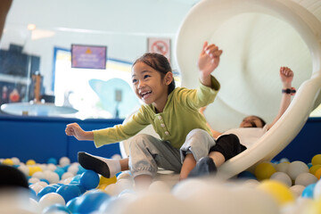 Exciting Slide Adventure. Happy girl sliding down into colorful ball pit, expressing joy and...