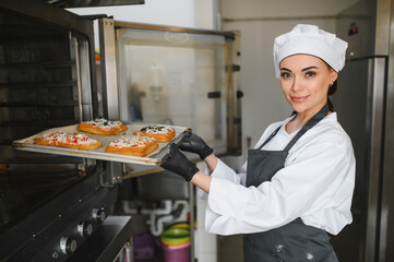 Baker taking tray of pastries out of oven in bakery