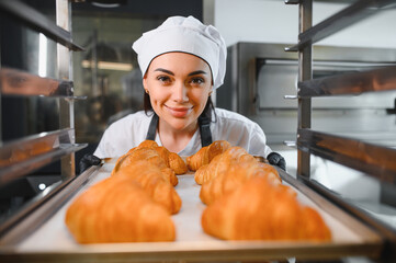 Baker placing tray of freshly baked croissants into industrial oven