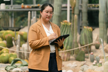 Scientist woman using smart tablet to research cactus species in greenhouse garden. Modern...