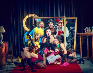 Ensemble of cabaret performers in colorful vintage costumes and dramatic makeup pose theatrically around large gold frame on red carpet. Concept of cabaret, show, circus, retro, vintage