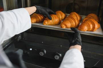 Baker taking freshly baked croissants out of oven