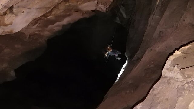 A caver, using Single Rope Technique, descends into a vast, dark opening within Anxiety State Cave, Chiang Mai, Thailand. Their headlamp pierces the enveloping darkness