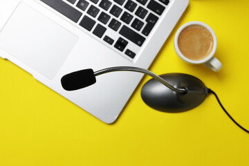Professional microphone, laptop and coffee on yellow background, flat lay