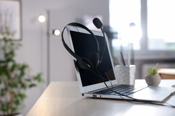 Headset with microphone and laptop on white wooden desk in office