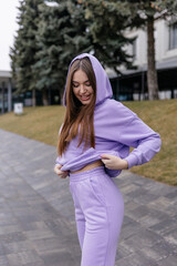 Cute girl model in a sporty comfortable casual purple outfit with a hoodie and sweatpants posing