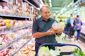 Elderly man chooses chicken meat in supermarket