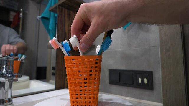 A man takes a toothbrush in his hand, multi-colored toothbrushes spin on the table. Slow motion