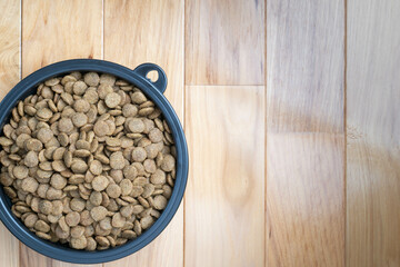 Crunchy, dry pet food or kibble in a black bowl on hickory, hardwood flooring.