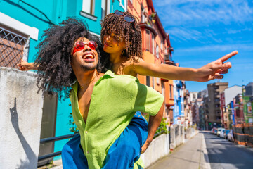 Obraz premium Young couple piggybacking and pointing in colorful city street