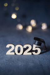 Wooden number 2025 with graduation hat on dark background with bokeh