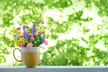 Beautiful still life with meadow flowers in cup on wooden table, green natural abstract background. Summer season. floral composition in rustic style. copy space
