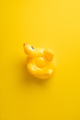 Bright vertical yellow inflatable duck toy featured on a bold yellow backdrop conveying summer vibes